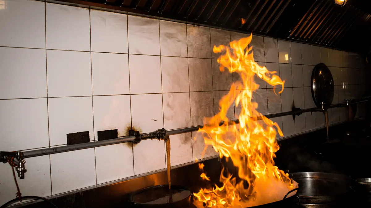 Grease fire flaring up along a kitchen wall pipe near a hood system
